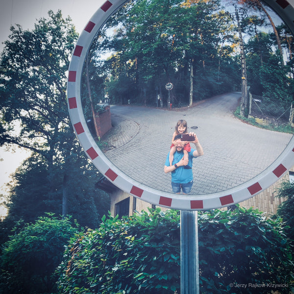 A father holding his daughter in his arms reflected in a traffic mirror. 