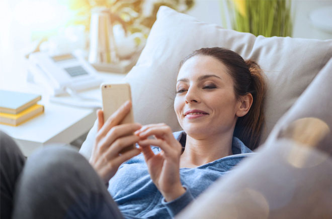 A lady lying on a couch while playing with her mobile phone