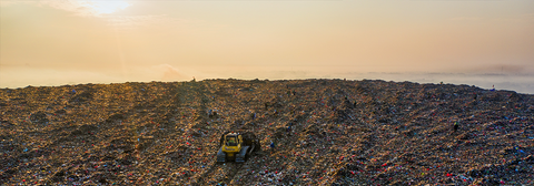 A large landfill with a yellow landfill bulldozer in the center.