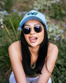 Girl wearing blue butterfly trucker hat and hexagon silver sunglasses