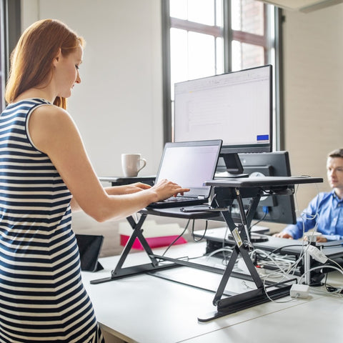 woman working on a sit-stand desk converter