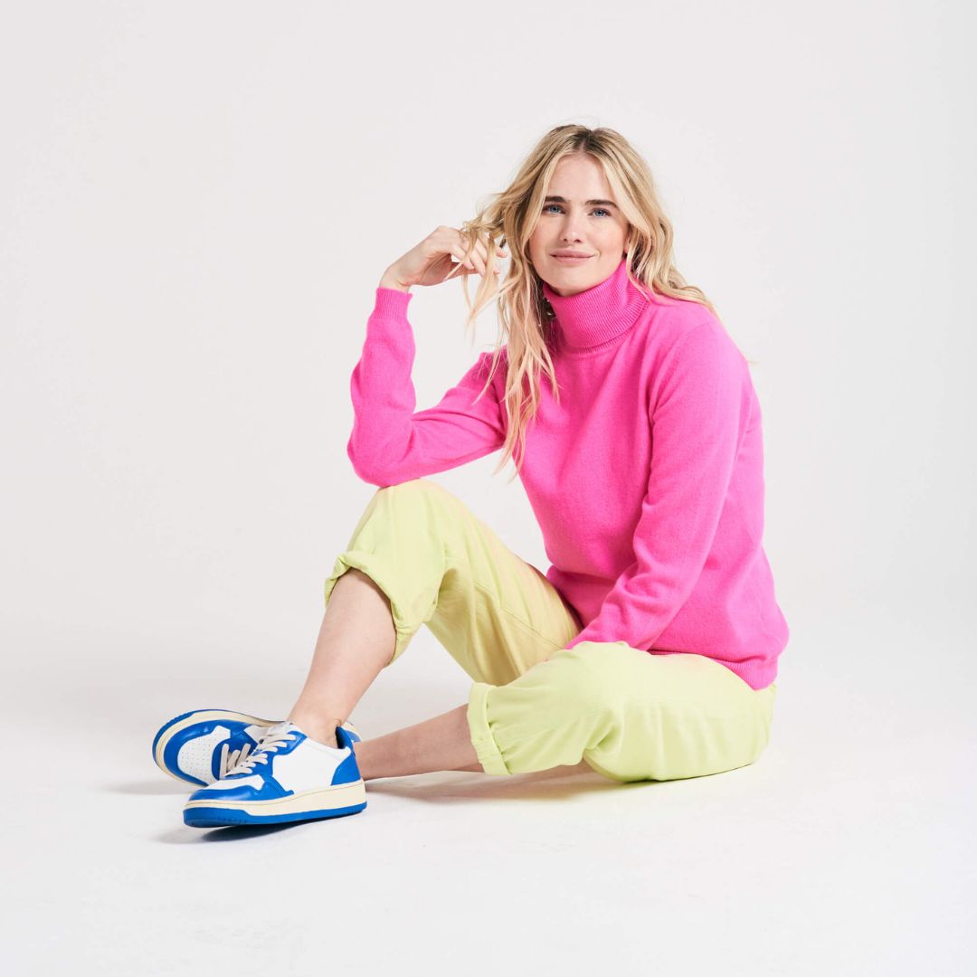 Pink roll neck jumper on model with blonde hair sitting on the floor