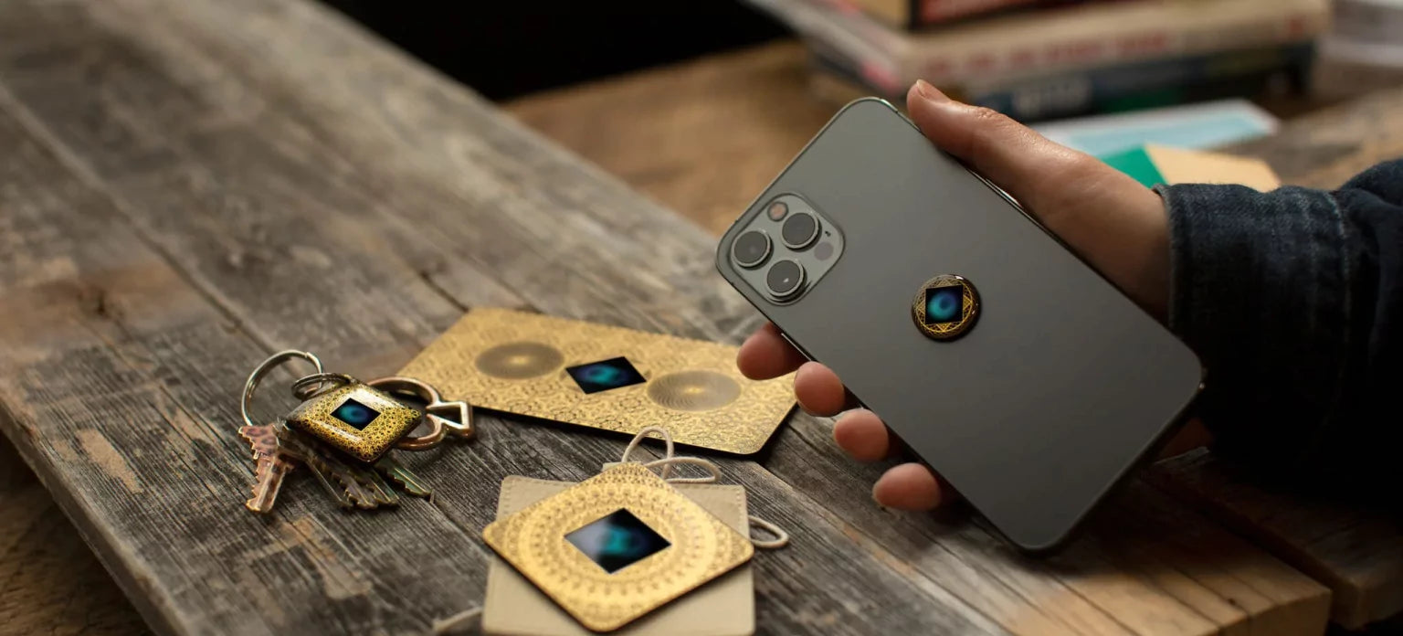 Person holding a smartphone with a decorative keychain and cards on a wooden surface.