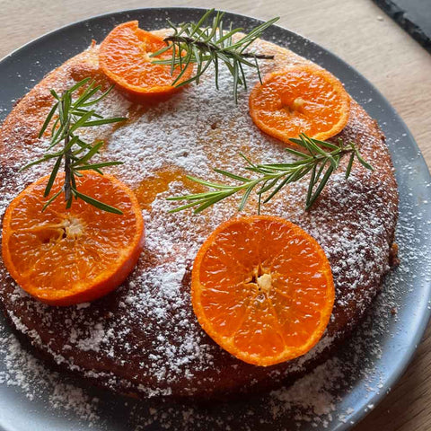 gluten free round sponge cake, dusted with icing sugar & decorated with slices of clementines & sprigs of thyme