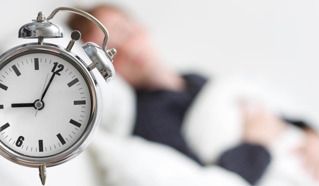 A clock looking at the camera while a person sleeps. 