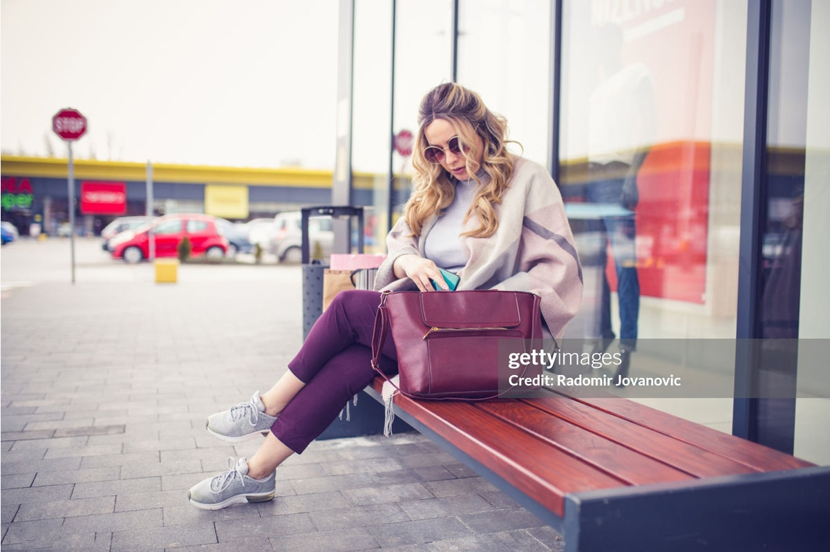 A lady is sitting on a bench with her neat tote bag beside her.