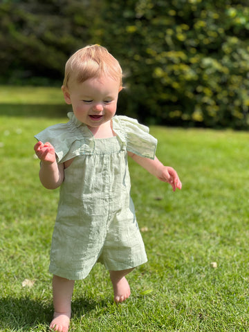 laughing toddler running on grass in sunshine wearing green romper