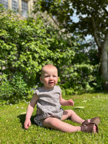 baby sat on lawn in summer wearing grey bubble