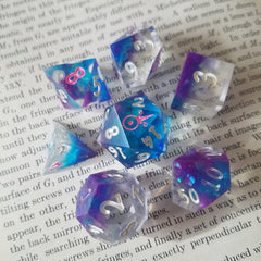 A set of dice containing iridescent flakes and a small layer of blue and purple resin at one end.