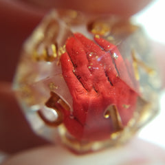 A macro photo of a red hand encased in a d10 die with gold foil flakes.