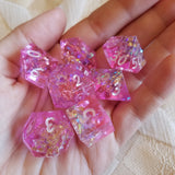 A set of sparkly pink dice sitting on someone's hand.