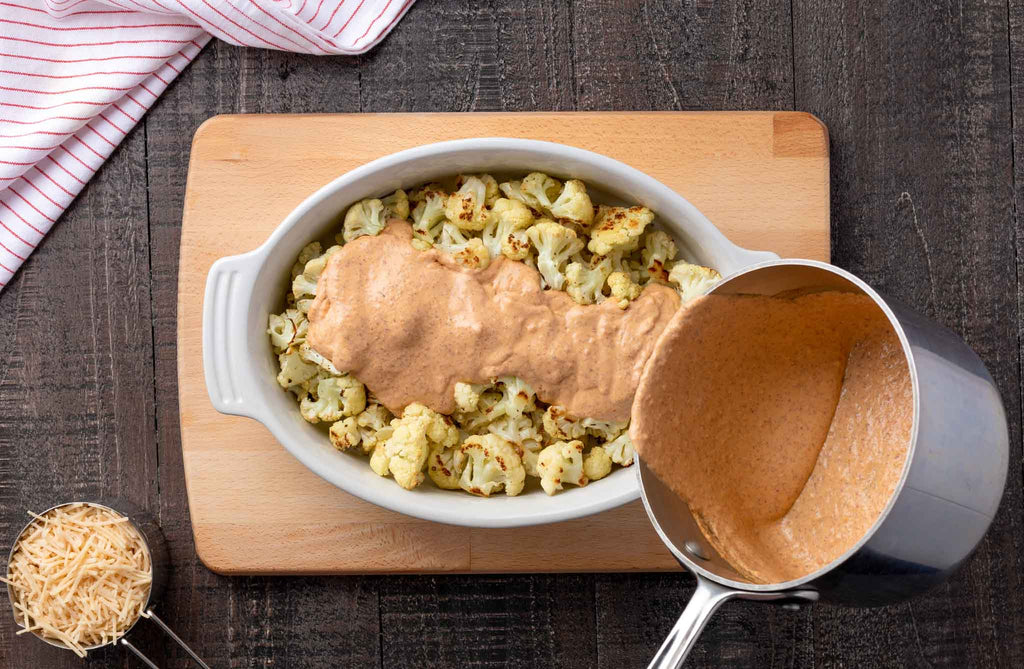 Pouring cheez mixture over cauliflower in baking dish