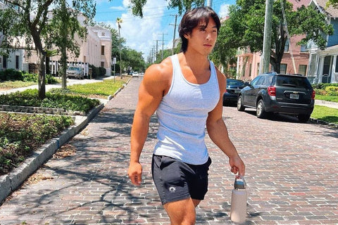 muscly man wearing tank top and black sol gym shorts walking down a street