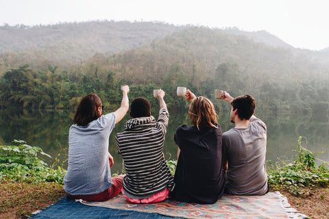 Group of people cheers their mugs of coffee on top of a mountain after a hike