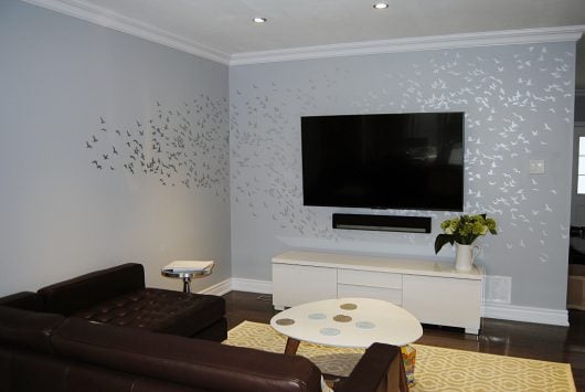 A DIY stenciled accent wall in a living room using the Flock of Cranes birds wall pattern from Cutting Edge Stencils in metallic silver over gray. http://www.cuttingedgestencils.com/products/bird-flock-wall-stencil-pattern