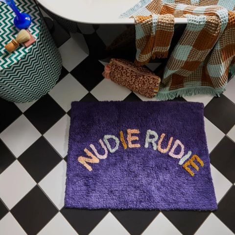 Nudie Rudie Bathmat in indigo with multi coloured lettering on checkered bathroom floor