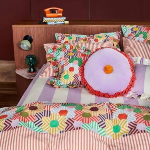 Retro maximalist bedroom with patterned bedlinen and sage and clare round cosimo pom pom cushion on bed
