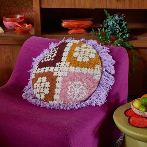 Vintage purple armchair in colourful living room with round patterned needle punch cushion on chair