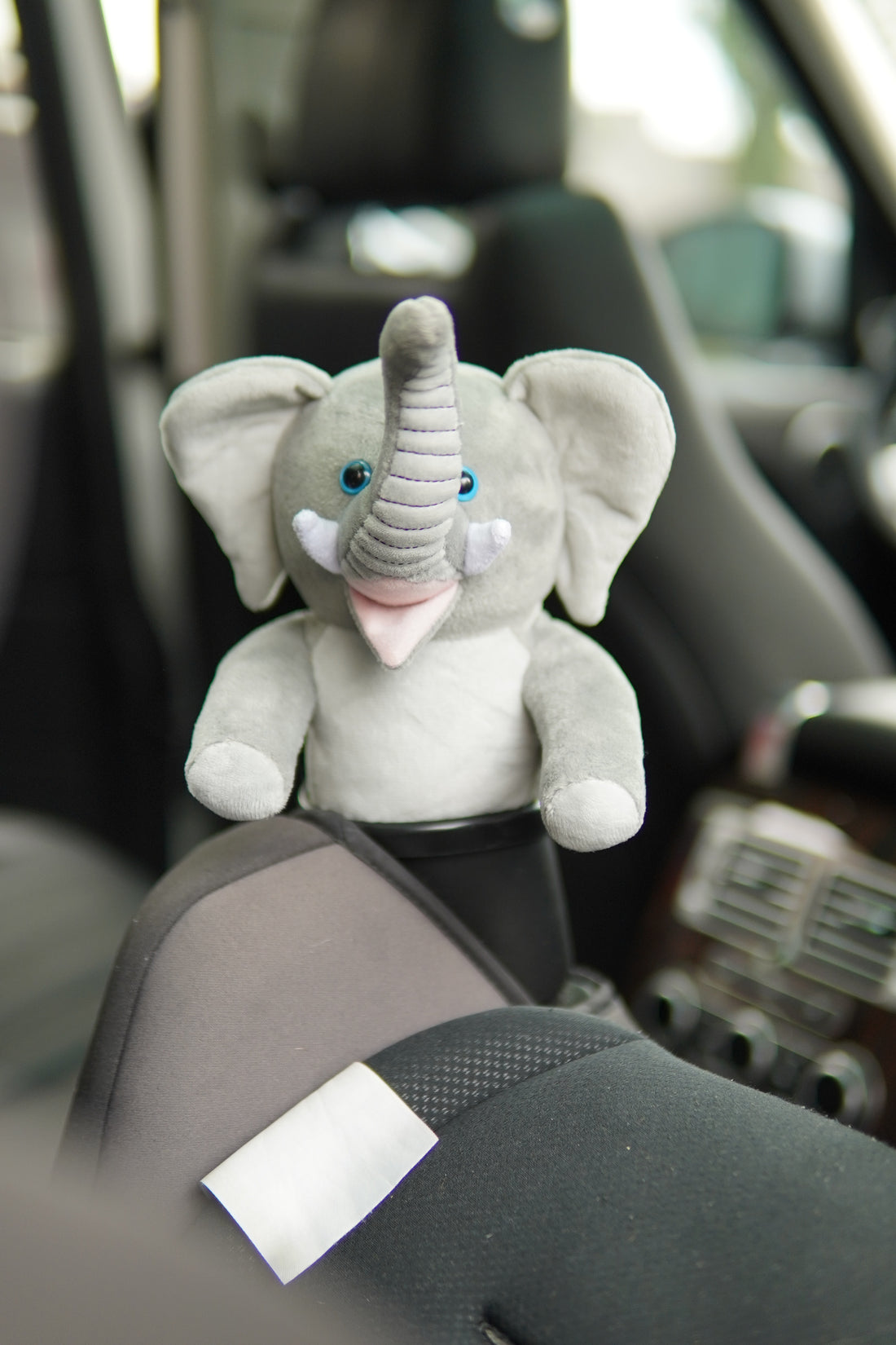 A gray elephant stuffed animal in a carseat cupholder. 