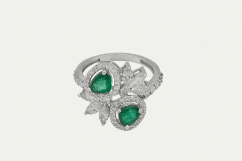 Our Emerald Ring is a floral design crafted in 18K White Gold set with 52 small round brilliant diamonds totaling 0.65 carats, 6 marquise cut diamond stones weighing 0.7 carats and two emerald stones totaling 0.95 carats