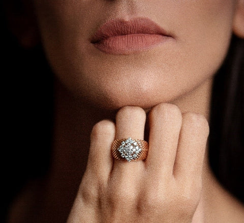 The Chevron Ring is an 18K rose gold ring with an intricate geometric design  adorned with 0.78 carats of 24 round diamonds surrounding a 0.12  carat brilliant diamond in the center