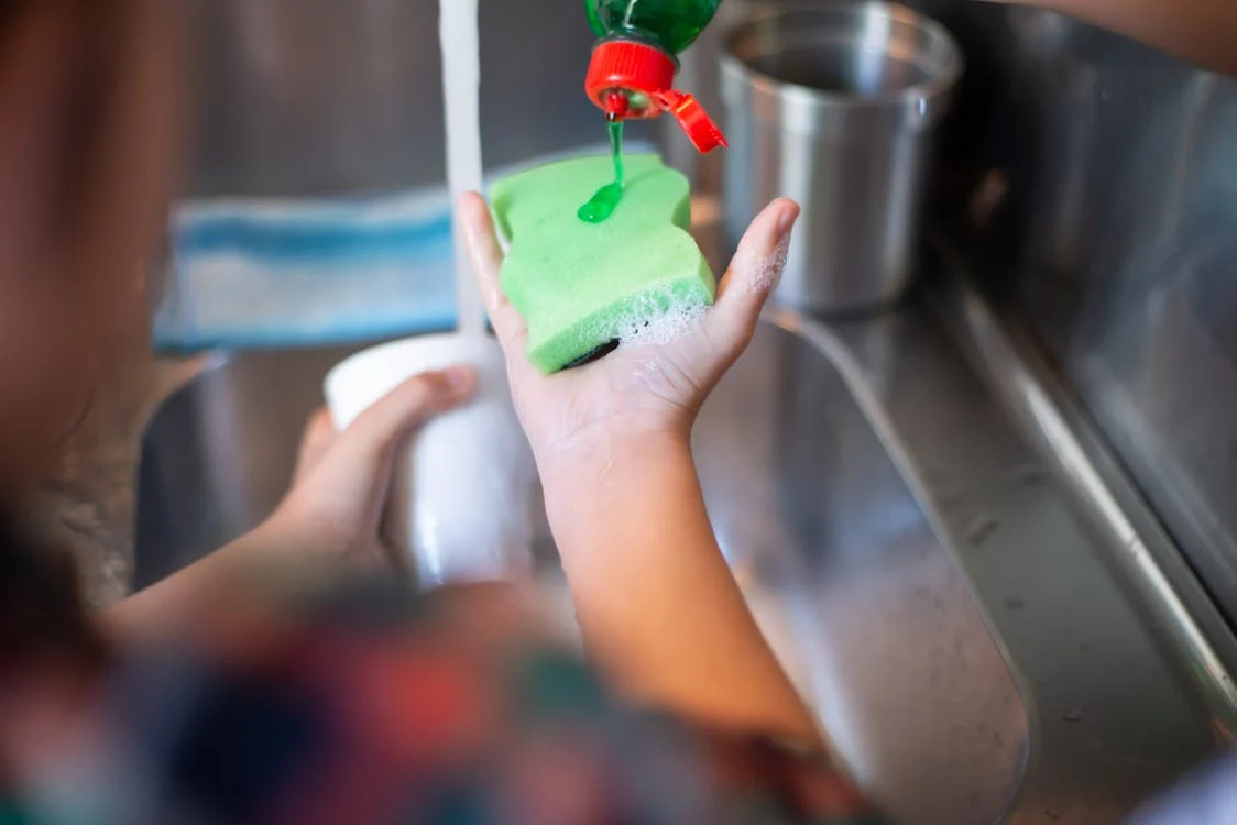 close up of a person washing a tumbler mug with dish soap and sponge
