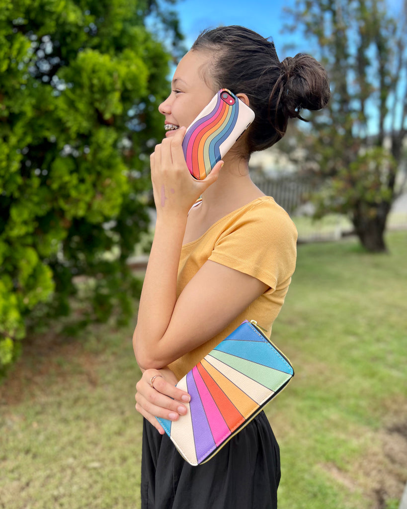 girl with a mobile phone on her ear, holding zip up wallet with a retro sun rays print on it | Raiana's Vibes