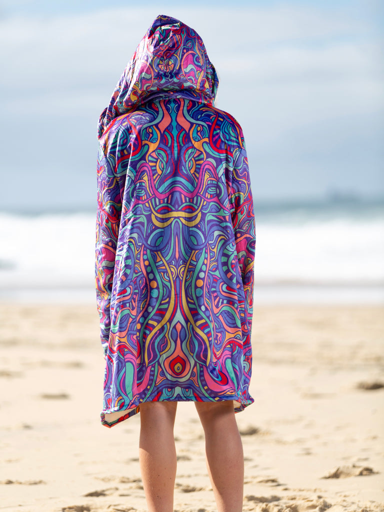 Rear view of a person wearing a cloak with a psychedelic pattern at the beach | Raiana's Vibes