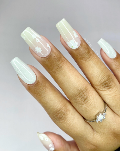 Close up photo of a manicure on a white background with semi cured gel nails. A white and clear floral pikake pattern with shimmery white accents
