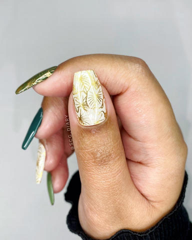 A close up of a hand with a semi cured gel manicure featuring a gold, white and green theme with kalo (taro) leaf pattern