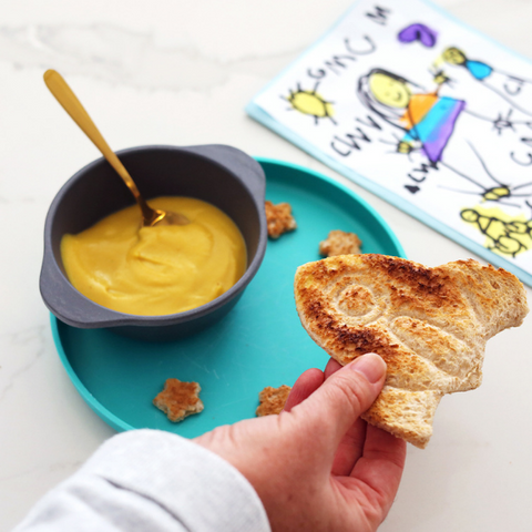 Childs hand playing with bread shaped as an aeroplane while eating soup