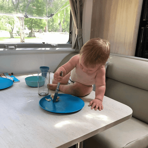 child sitting on a table inside a caravan playing with a bamboo plate