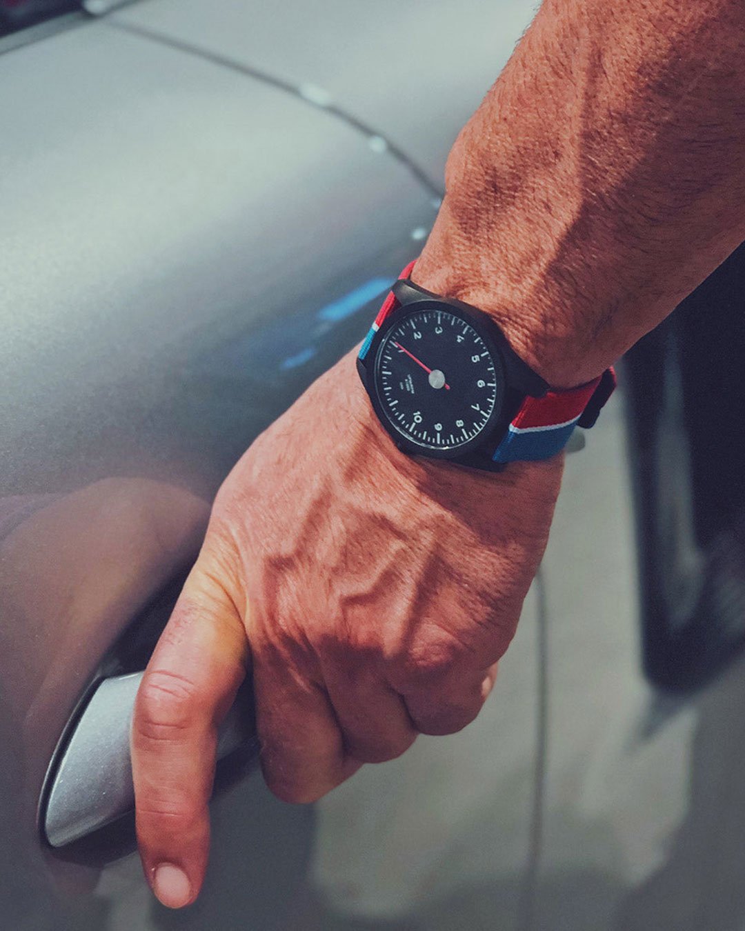 A person holding a car door handle wearing an GRD watch