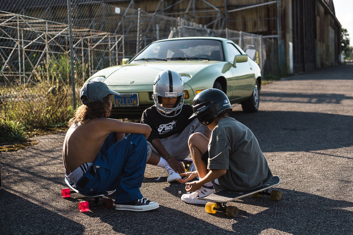 A group three riders sitting on skateboards with a Porsche in the background