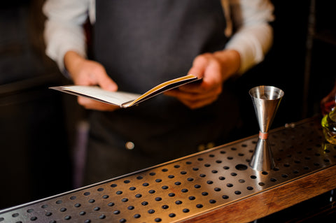 Bar tender behind bar with a recipe book