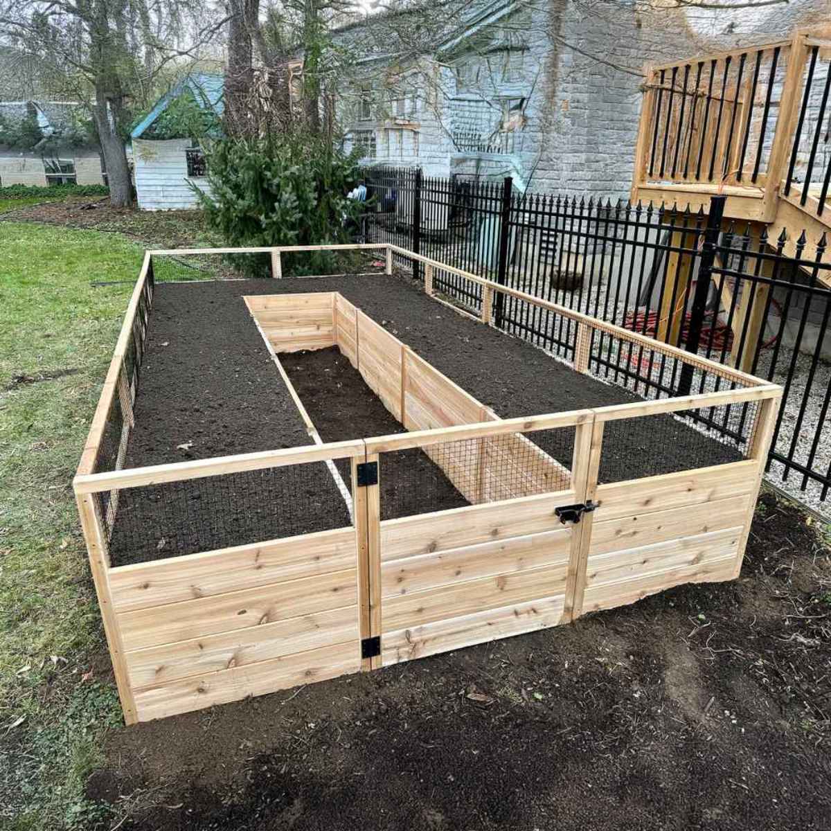 A large rectangular garden bed with fresh soil and a central walkway shows a practical example of How to Fill Raised Garden Beds in a spacious yard