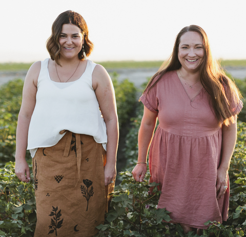 two women, smiling, standing in a field. 