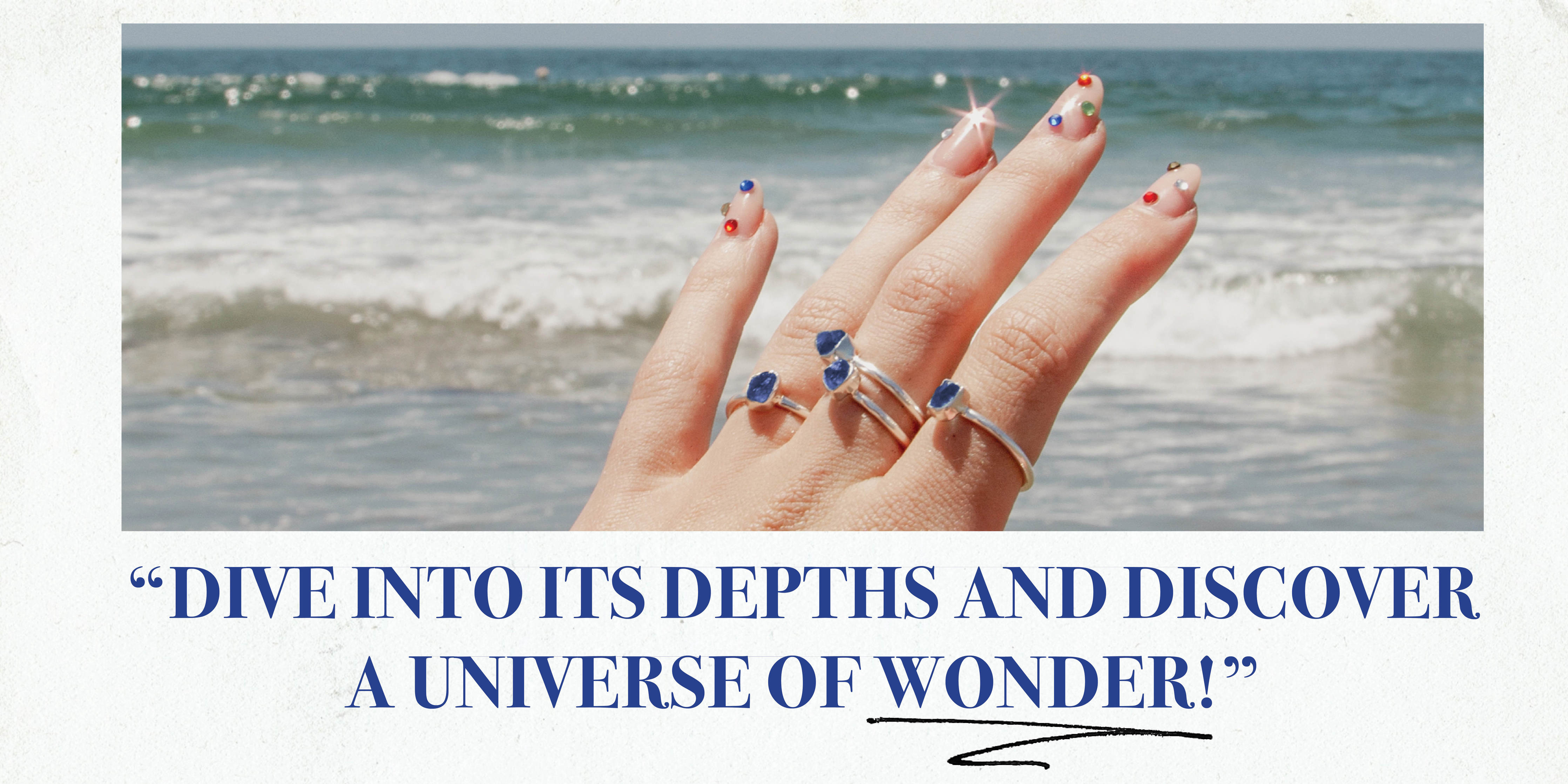 Image of a hand with many silver and sapphire rings with an ocean backdrop with text saying, Dive into its depths and discover a universe of wonder!