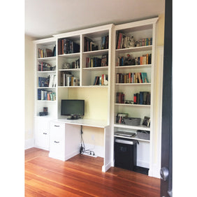 Custom full wall shelving and desk unit, with adjustable shelves and cabinets, and two drawers in the desk. Shown finished in white.