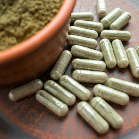 Green supplement capsules next to a bowl of green wheatgrass powder