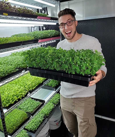 CJ Vaughn of on the grow holding Pea Microgreens in front of our Grow Rack