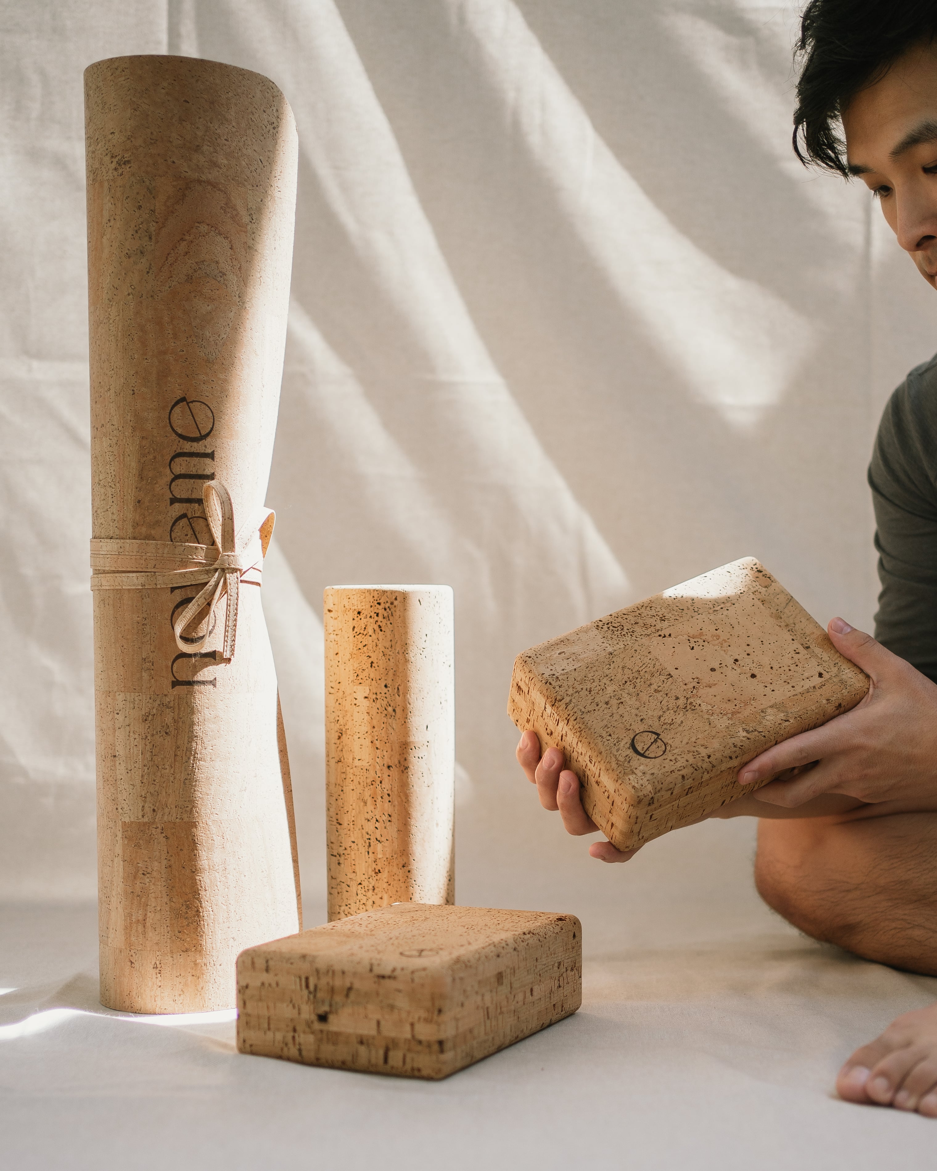 model holding a noveme cork yoga block next to another block, a roller and a cork yoga mat