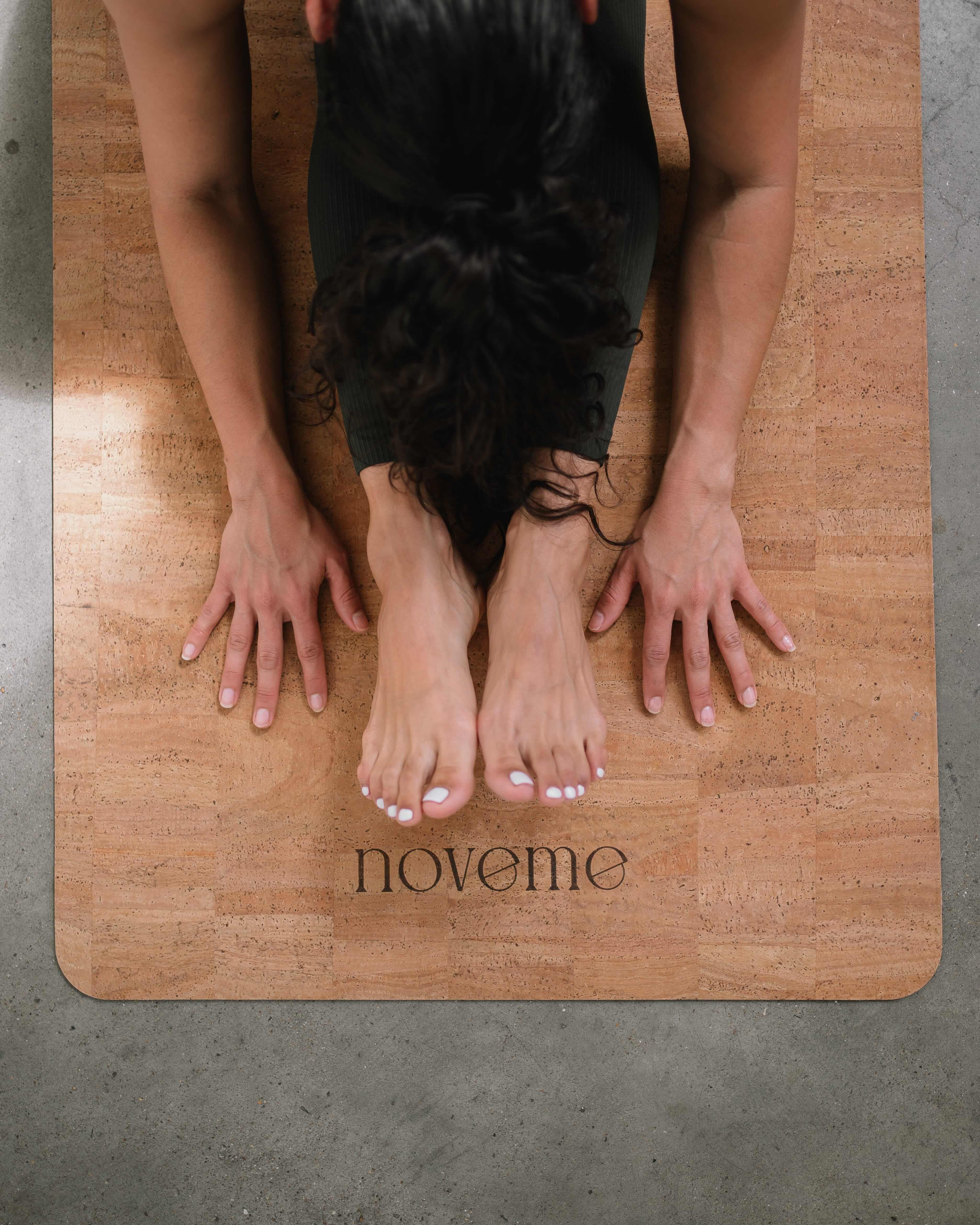 woman doing a seated forward fold on a Noveme Cork Yoga mat 