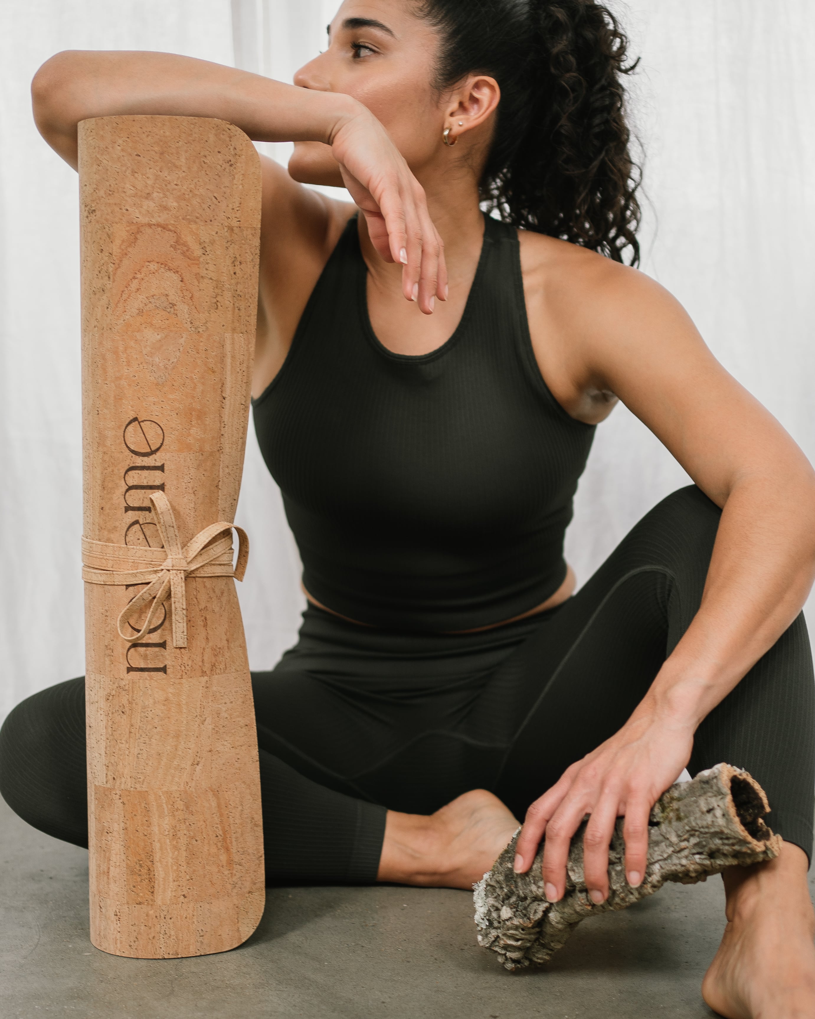 model seated next to a noveme cork yoga mat holding a piece of cork