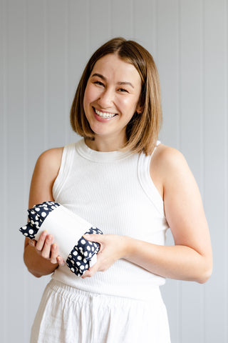 Natalie standing and smiling holding a heat pack that is navy with white spots.
