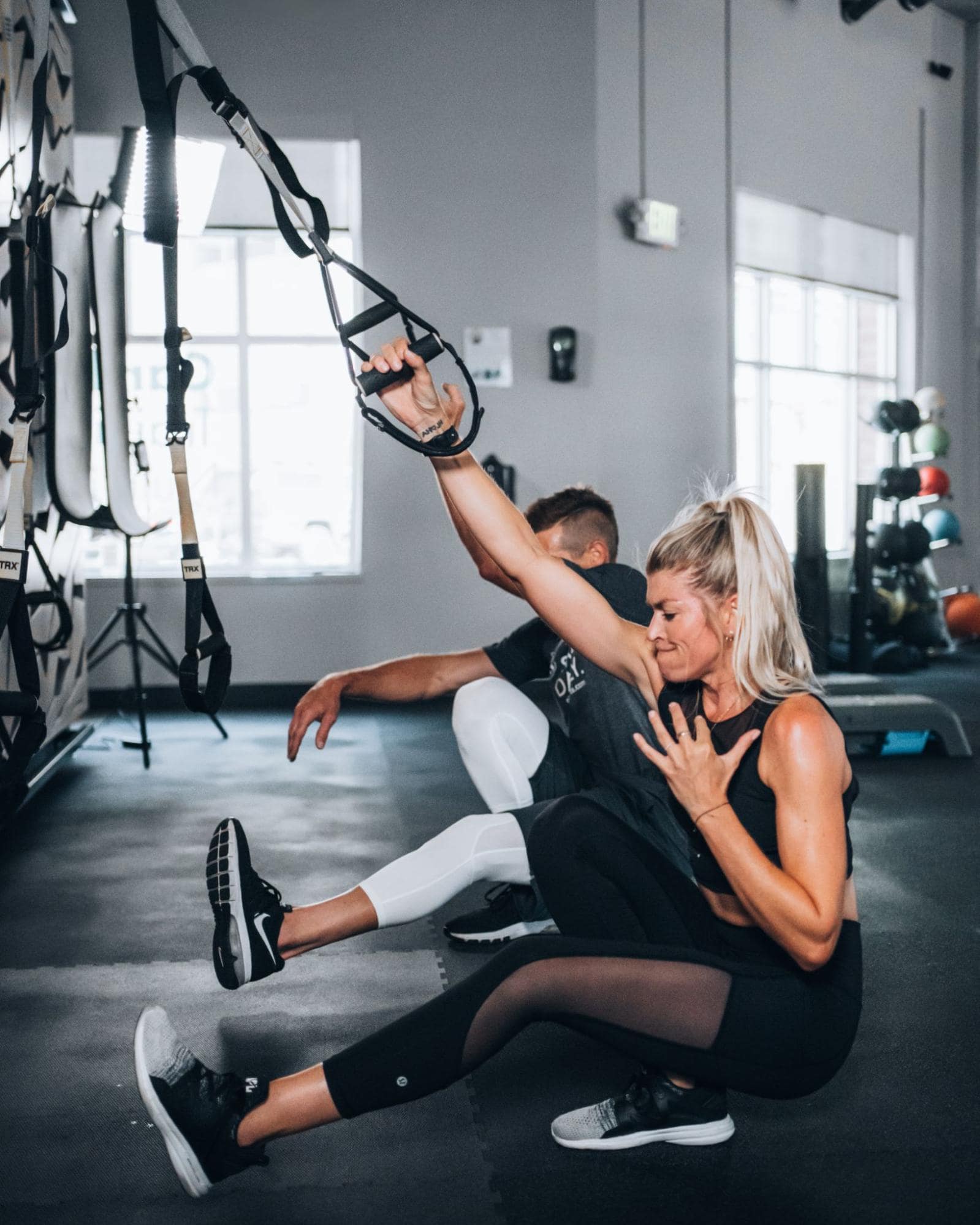 Woman and man pistol squatting with TRX bands