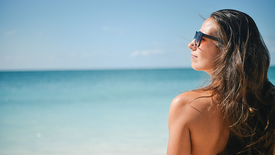 A young woman at the beach with sunglasses, looking at the horizon