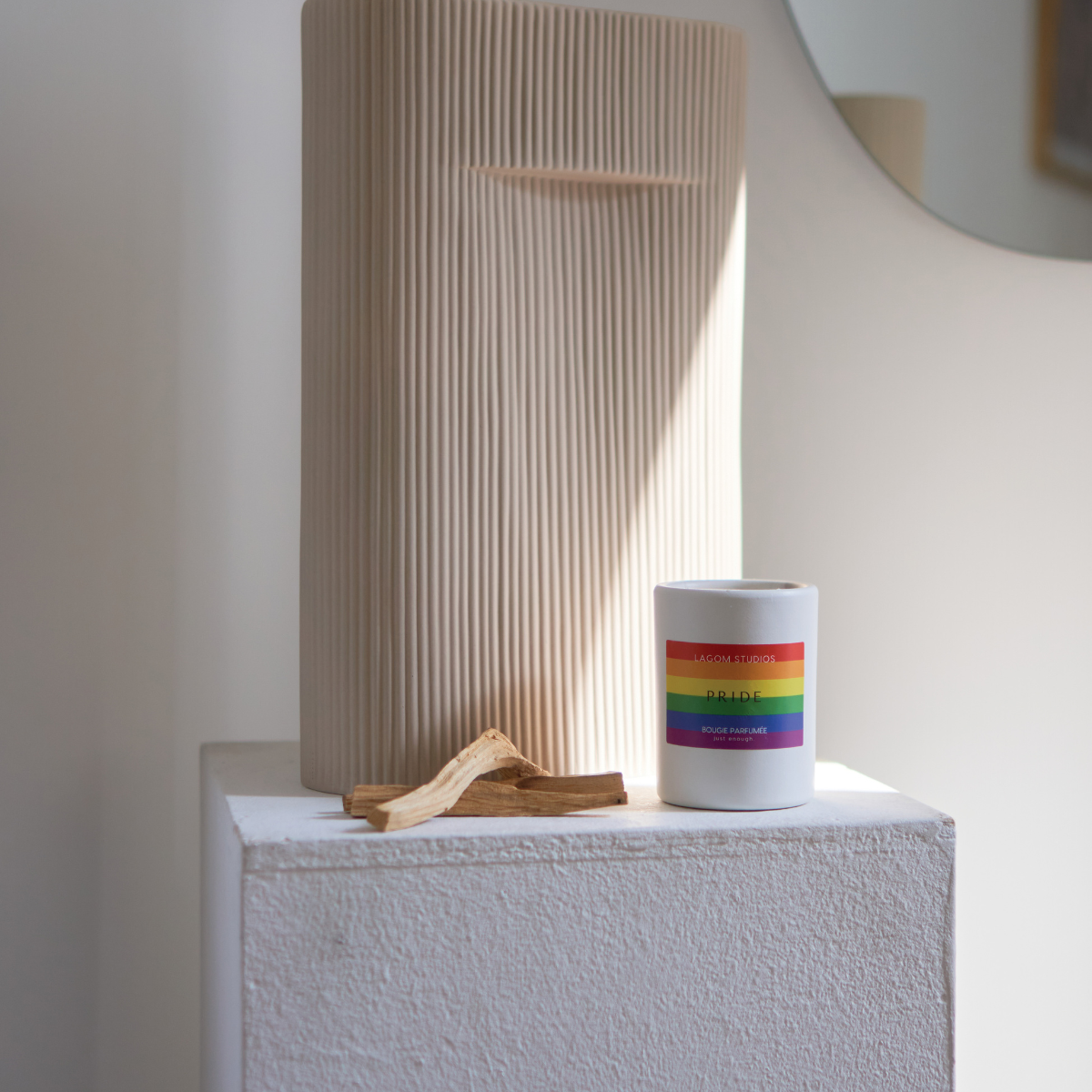 Lagom Studios_Vegane Duftkerze PRIDE in weißem Keramikgefäß auf Sockel im Wohnzimmer vor geriffelter Vase