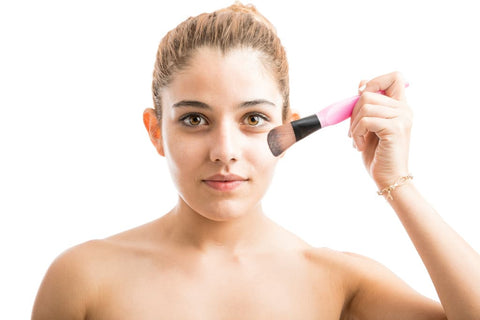 A woman using a brush to apply product to her face