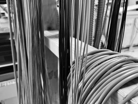 Black and white image of several cables of varying lengths and colors hanging on a stand